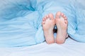 Men`s feet sticking out from under the blue blanket.