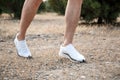 Men`s feet in white sneakers running over rough terrain. Cross country running with focus on runner`s legs