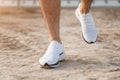 Men`s feet in white sneakers running over rough terrain. Cross country running with focus on runner`s legs