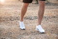 Men`s feet in white sneakers running over rough terrain. Cross country running with focus on runner`s legs