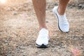 Men`s feet in white sneakers running over rough terrain. Cross country running with focus on runner`s legs