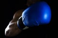 Men`s hand in a blue boxing glove on a black background makes a punch