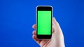 Men`s hand holding the smartphone in a vertical position. Green screen on the phone and blue chromakey. Mobile ads