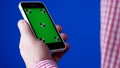 Men`s hand holding the smartphone in a vertical position. Green screen on the phone and blue chromakey. Tracking markers