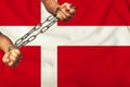 Men`s hands chained in heavy iron chains against the background of the flag of Denmark on a gentle silk with folds in the wind,