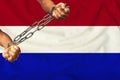 Men`s hands chained in heavy iron chains against the background of the flag of Holland on gentle silk with folds in the wind,