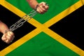 Men`s hands chained in heavy iron chains against the background of the flag of Jamaica on a gentle silk with folds in the wind,