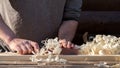 Men`s hands close-up planing a board on a workbench with a pile of shavings on the background of a dark wall of the house with a