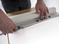 Men`s hands cut off white blank wallpaper without pattern using blue cutter knife,construction ruler with level gauge