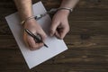 Men`s hands with handcuffs fill the police record, confession. Royalty Free Stock Photo