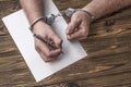 Men`s hands with handcuffs fill the police record, confession. Royalty Free Stock Photo