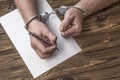 Men`s hands with handcuffs fill the police record, confession. Royalty Free Stock Photo