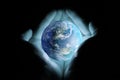 Men`s hands holding the planet earth with a blue glow on a black background.