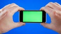 Men`s hands holding the smartphone in a horizontal position. Green screen on the phone and blue chromakey. No gesturing