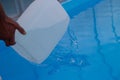 Men`s hands pour light liquid from a plastic tank into a pool, into water. chemical water purification, alkali balance, unsanitar