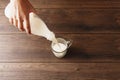 Men`s hands pour milk from a bottle into a glass, close-up, top view. Brown wooden table Royalty Free Stock Photo