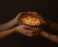 Men`s hands and women`s hands with a tattoo holding a nest of branches with yellow garlands around a dark background. Royalty Free Stock Photo