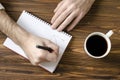 Men`s hands writing in notepad and cup of coffee on wooden ta