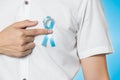 Men`s healthcare concept - close up of male hand pointing to light blue ribbon for prostate cancer at left chest on blue Royalty Free Stock Photo