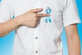 Men`s healthcare concept - close up of male hand pointing to light blue ribbon for prostate cancer at left chest on blue Royalty Free Stock Photo