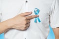 Men`s healthcare concept - close up of male hand pointing to light blue ribbon for prostate cancer at left chest on blue Royalty Free Stock Photo