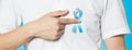 Men`s healthcare concept - close up of male hand pointing to light blue ribbon for prostate cancer at left chest on blue Royalty Free Stock Photo