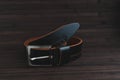 Men's leather trouser belt in black on a dark background of old wood.