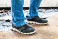 Men`s legs in blue jeans and black sneakers with white soles stand on a dirty oiled ground. Dirty car master workplace Royalty Free Stock Photo