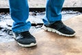 Men`s legs in blue jeans and black sneakers with white soles stand on a dirty oiled plywood board. Dirty car master workplace Royalty Free Stock Photo