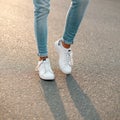 Men`s legs in blue stylish jeans in white fashionable sneakers on the background of asphalt. Close-up Royalty Free Stock Photo