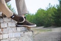 Men's legs in the brown shoes sneakers. Man sitting on the old brick wall outdoor.