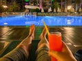 Men`s legs on a deck chair by the pool at night, relaxing with an alcoholic cocktail in a hotel in a warm eastern tropical countr Royalty Free Stock Photo