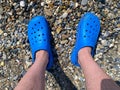 Men`s legs, feet in blue rubber slippers against the background of pebbles and sand on a vacation on the beach in a warm tropical Royalty Free Stock Photo