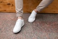 Men`s legs in leather fashion white sneakers in stylish beige pants. Trendy casual outfit. Details of everyday look.