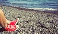 Men`s legs in shorts and red sneakers on a pebbly beach by the sea on a sunny day. Royalty Free Stock Photo