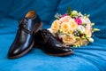 Wedding rings lie on men`s shoes, next to a beautiful wedding bouquet on a blue background Royalty Free Stock Photo
