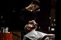 Men`s style. The barber dressed in a black clothes scissors beard of brutal man in the stylish barbershop