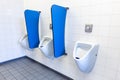 Men's urinals on white wall with blue partitions