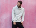 Men`s youth street fashion. Gray hoodie and black pants on a young man posing against a pink wall background.