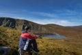 Men sitting on a rock and drinking coffee from thermos. Scenic view on Lough Ouler and Tonelagee Mountain, Ireland