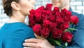 A man in a suit embraces a pretty girlfriend and gives her a luxurious bouquet of red roses. A romantic gift for Valentine`s Day, Royalty Free Stock Photo