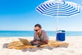 Young man using a laptop computer on the beach under solar umbrella. Freelance Concepts Royalty Free Stock Photo