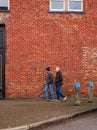 Men walking fast on the brick wall background in town. Urban infrastructure, people walking on a street in springtime