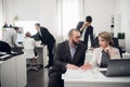 Men and woman discuss something, man talkson phone, other three work at a table on backgorund