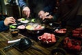 Men and women hands pinching medium rare slice Wagyu A5 beef and Kurobuta pork in hot pot shabu clear soup base by chopsticks.