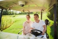 Happy couple rides on a white golf cart playing golf. The woman laid her hand on the man`s shoulder Royalty Free Stock Photo