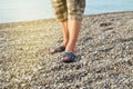 Men& x27;s feet in flip-flops and shorts, a man standing on the beach on a pebble beach, sunrise in the morning Royalty Free Stock Photo