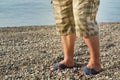 Men& x27;s feet in flip-flops and shorts, a man standing on the beach on a pebble beach, sunrise in the morning Royalty Free Stock Photo