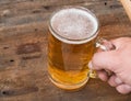 Men's hand holds a mug of light beer on dark vintage wooden boards Royalty Free Stock Photo