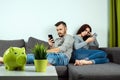 A man and a young woman, sitting on the couch and holding smartphones in their hands, turned away from each other. The concept of Royalty Free Stock Photo